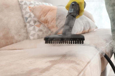 Photo of Janitor removing dirt from sofa with steam cleaner, closeup
