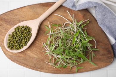 Wooden board with mung beans and sprouts on light table, top view