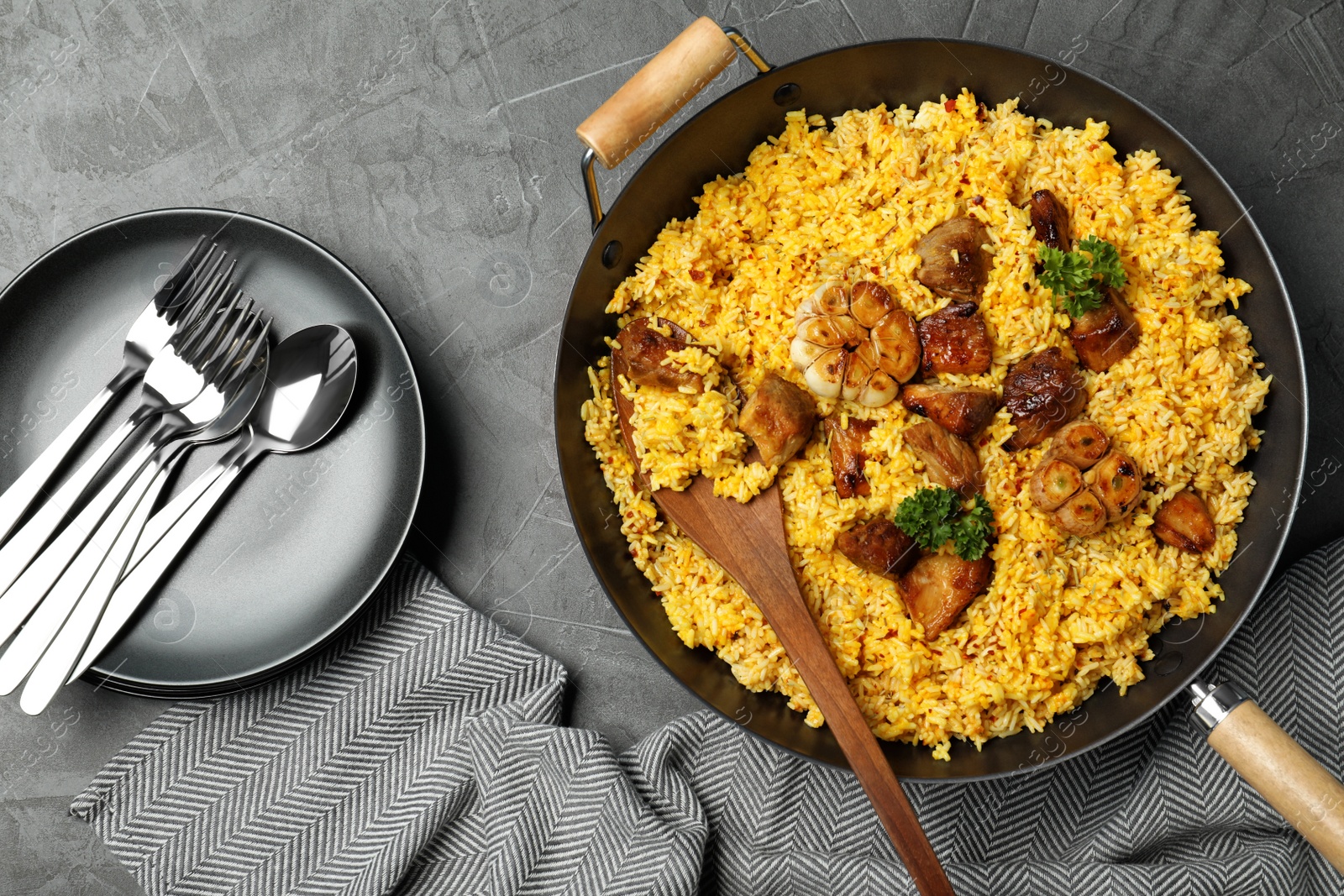 Photo of Frying pan with delicious rice pilaf and cutlery on grey background, flat lay