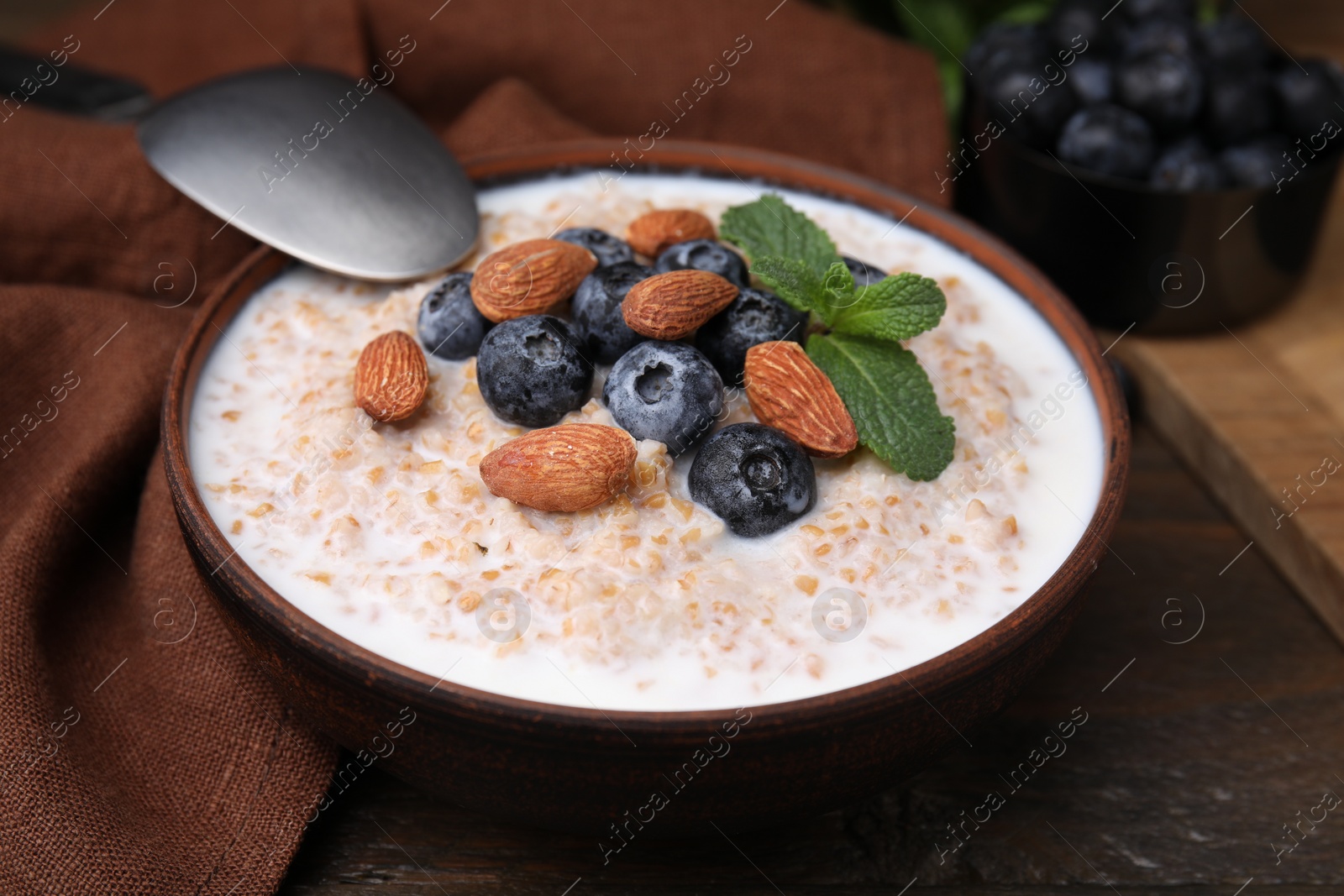 Photo of Tasty wheat porridge with milk, blueberries and almonds in bowl served on wooden table, closeup