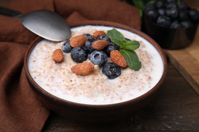 Photo of Tasty wheat porridge with milk, blueberries and almonds in bowl served on wooden table, closeup