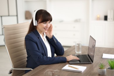 Photo of Woman in headphones watching webinar at wooden table in office