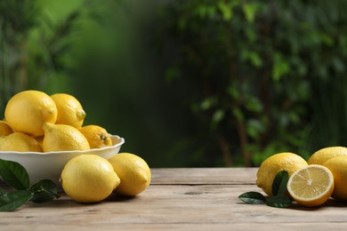 Photo of Fresh lemons and green leaves on wooden table. Space for text