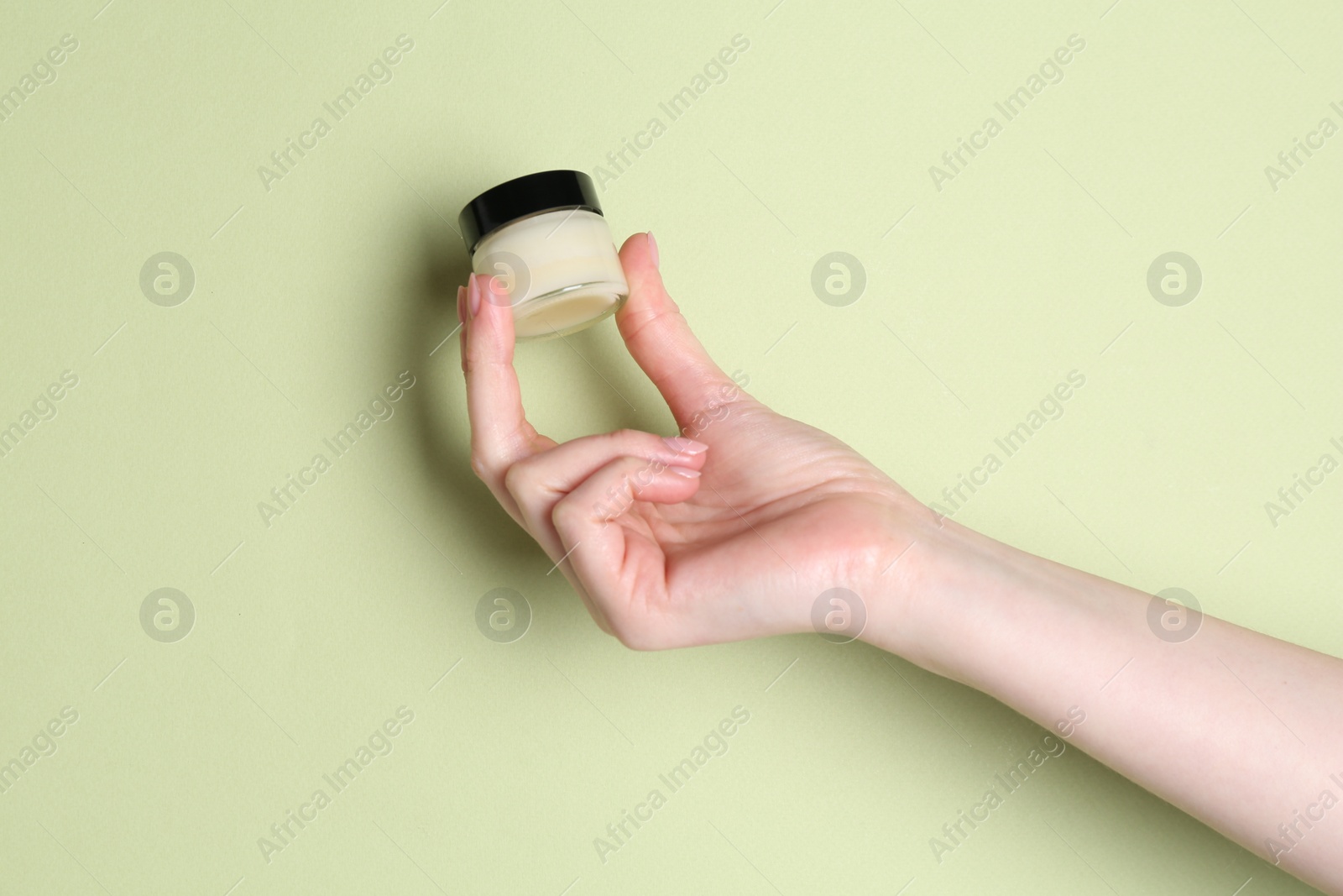 Photo of Woman holding jar of cream on green background, closeup