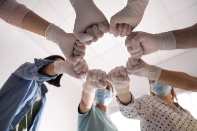 Photo of People in white medical gloves joining fists on light background, low angle view