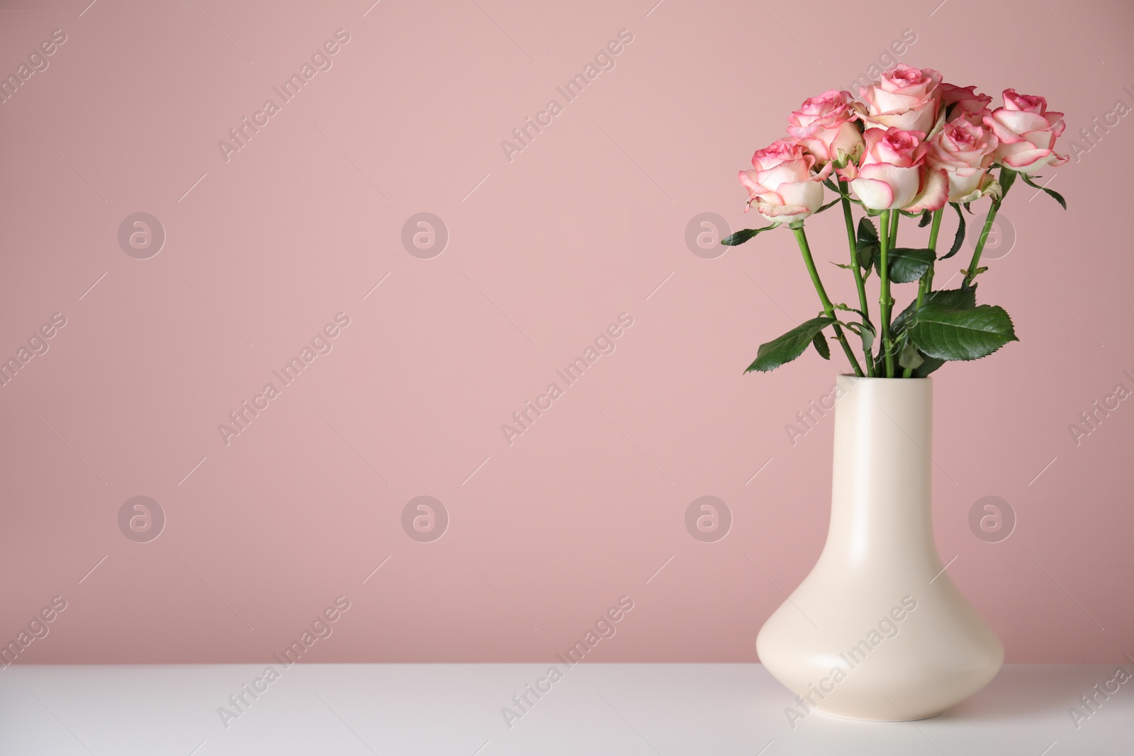 Photo of Vase with beautiful roses on white table against pink background. Space for text