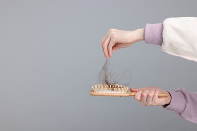Photo of Woman holding brush with lost hair on light grey background, closeup and space for text. Alopecia problem