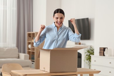 Photo of Emotional young woman with opened parcel at home. Internet shopping