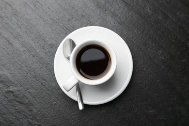 Photo of Hot coffee in cup, spoon and saucer on dark textured table, top view