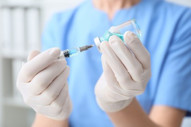 Doctor filling syringe with medication from vial on blurred background, closeup