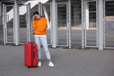 Photo of Being late. Worried young woman with red suitcase outdoors, space for text