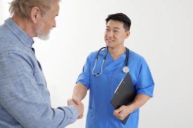 Happy doctor shaking hands with patient on white background