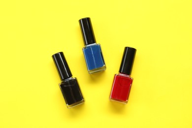 Photo of Colorful nail polishes in bottles on yellow background, flat lay