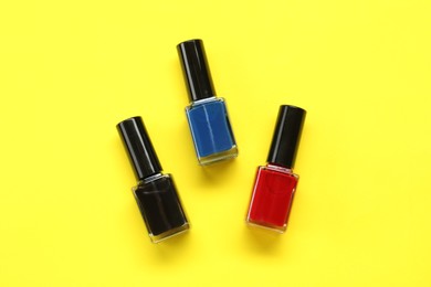 Colorful nail polishes in bottles on yellow background, flat lay