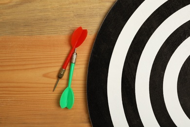 Dart board with color arrows on wooden background, top view