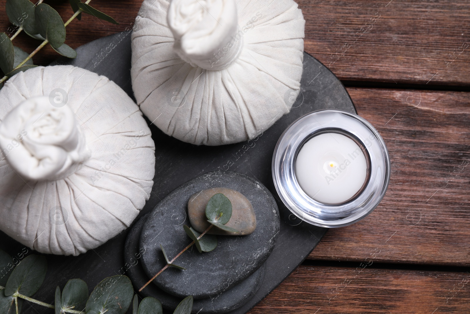 Photo of Beautiful spa composition with herbal massage bags, stones and eucalyptus branches on wooden table, flat lay