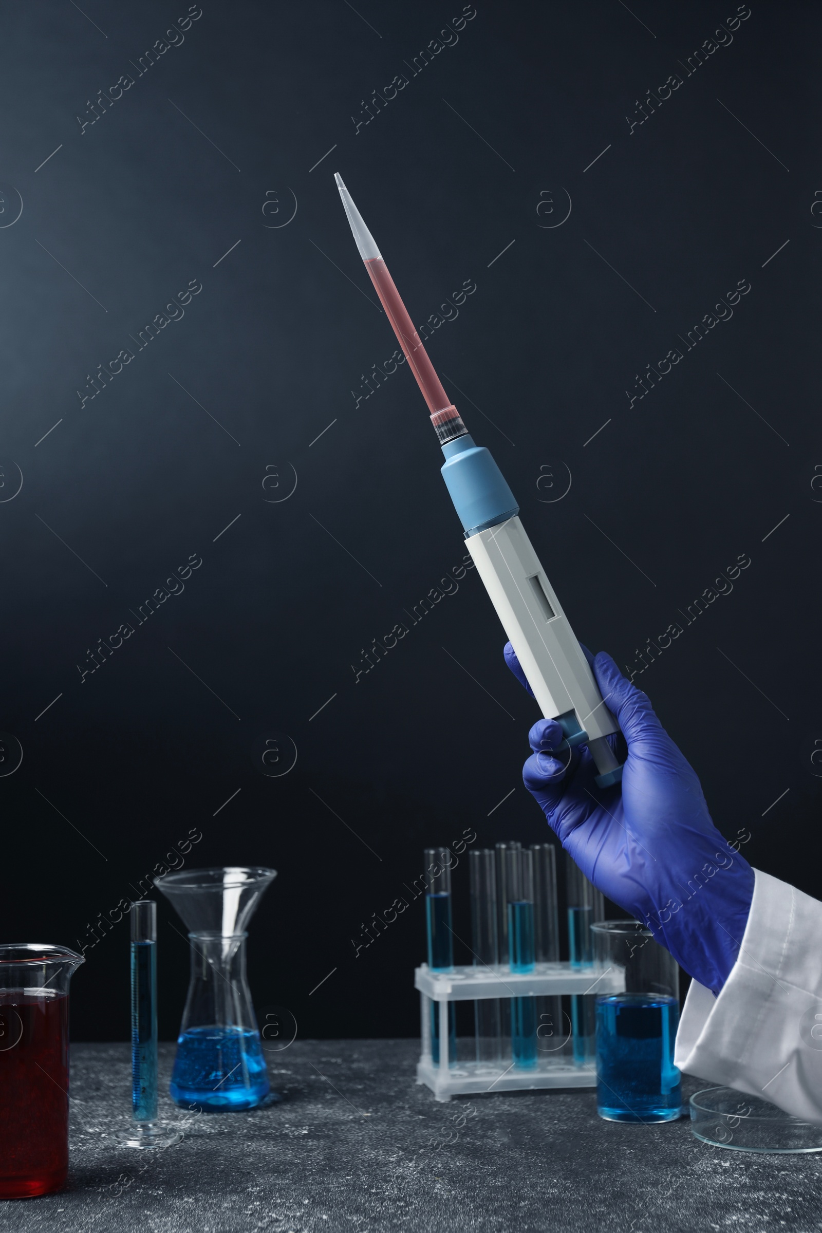 Photo of Laboratory analysis. Scientist holding micropipette with liquid at grey table, closeup