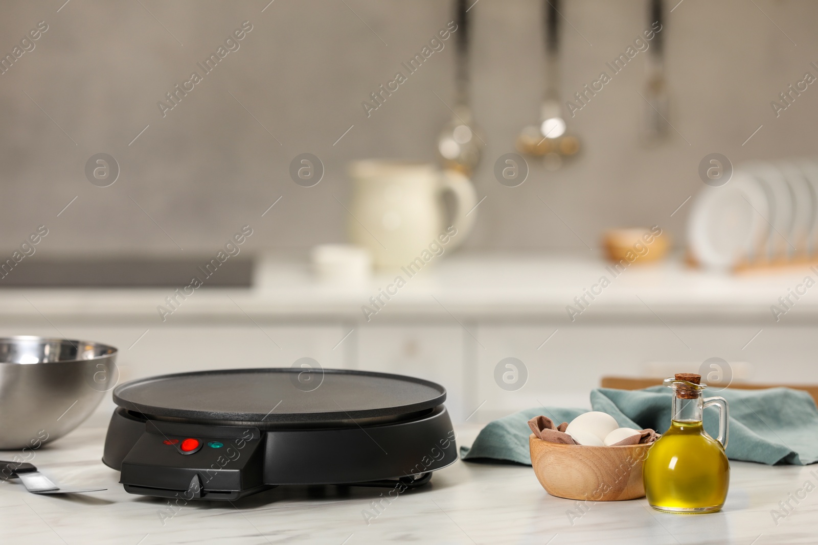 Photo of Electrical crepe maker and ingredients on white marble table in kitchen, space for text