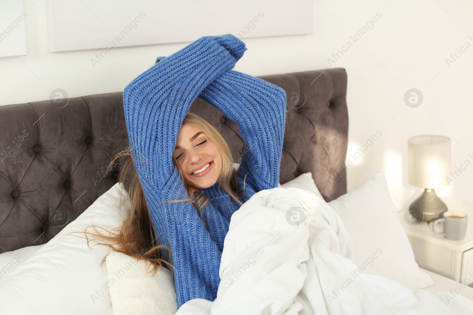 Photo of Beautiful young woman stretching in bed and smiling at home. Winter atmosphere