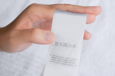 Photo of Woman holding clothing label on white garment, top view