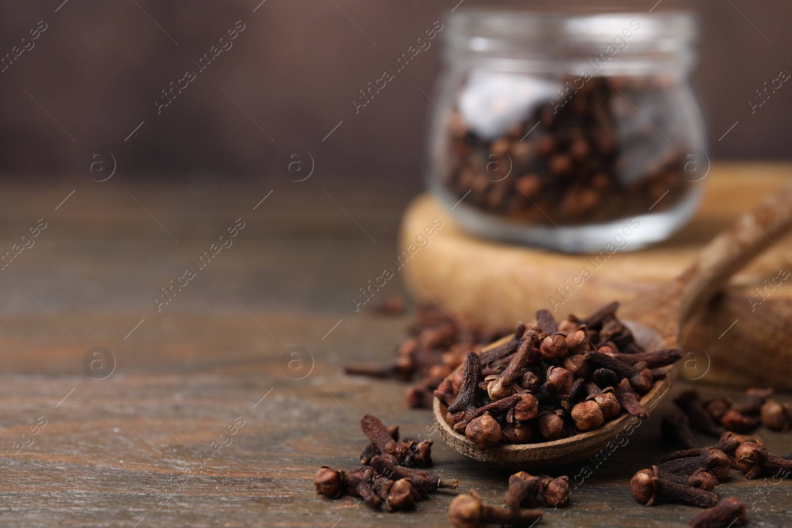 Photo of Spoon with aromatic cloves on wooden table, closeup. Space for text