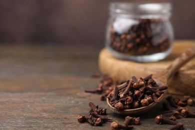 Spoon with aromatic cloves on wooden table, closeup. Space for text