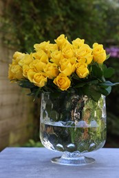 Photo of Beautiful bouquet of yellow roses in glass vase on light table outdoors