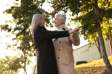 Photo of Affectionate senior couple dancing together outdoors, low angle view