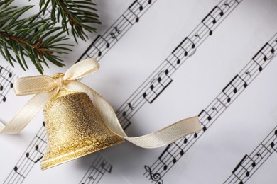 Photo of Golden bell with bow and fir branches on music sheets, flat lay. Christmas decor