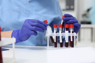 Laboratory testing. Doctor with blood samples in tubes at white table indoors, closeup