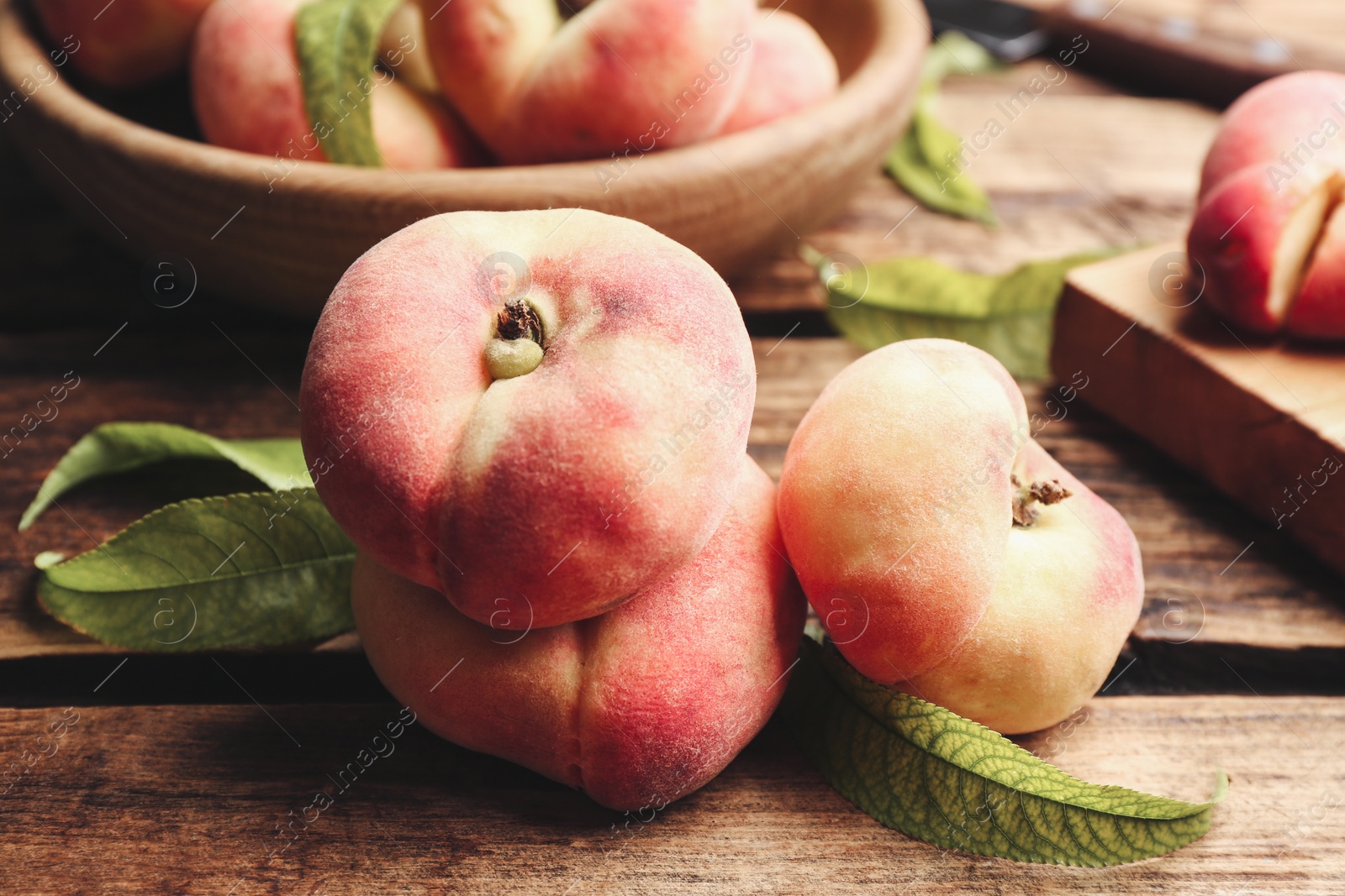 Photo of Fresh ripe donut peaches with leaves on wooden table, closeup