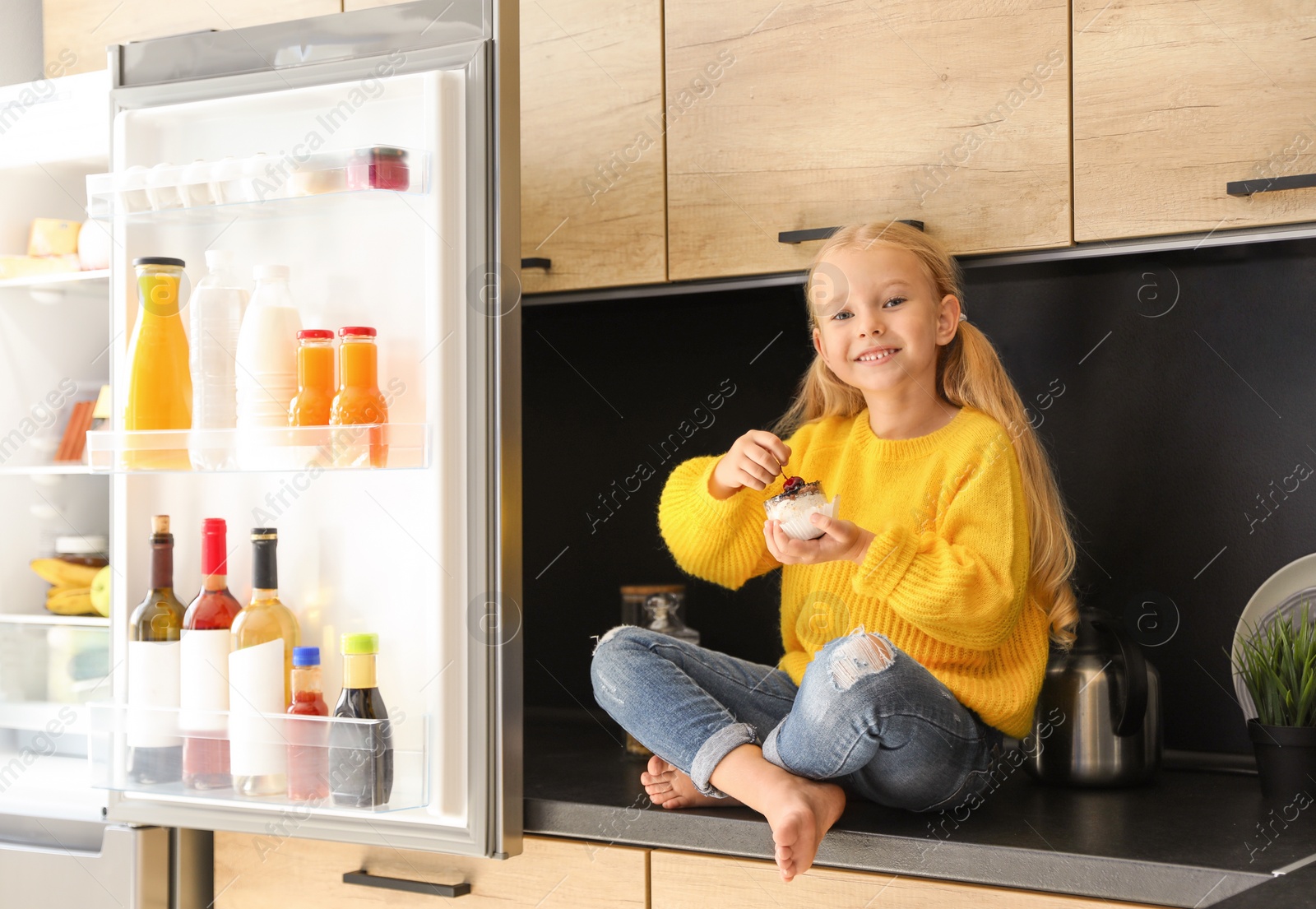 Photo of Girl eating dessert near refrigerator in kitchen