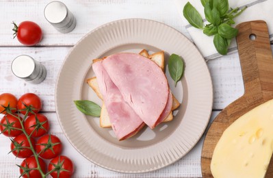 Photo of Delicious sandwich with ham, tomatoes and cheese on white wooden table, flat lay