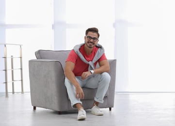 Handsome young man sitting in armchair indoors. Space for text