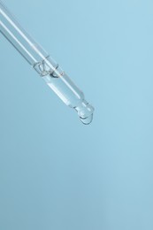 Dripping cosmetic serum from pipette on light blue background