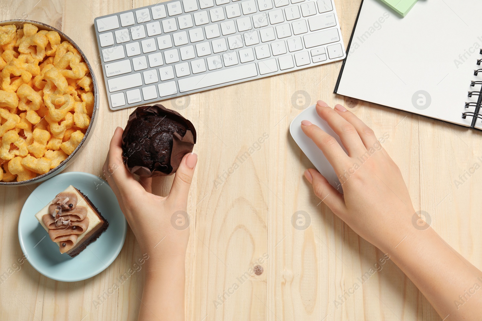 Photo of Bad habits. Woman eating muffin while working on computer at wooden table, top view