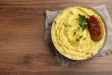 Bowl of tasty mashed potatoes with parsley, black pepper and cutlet served on wooden table, top view. Space for text