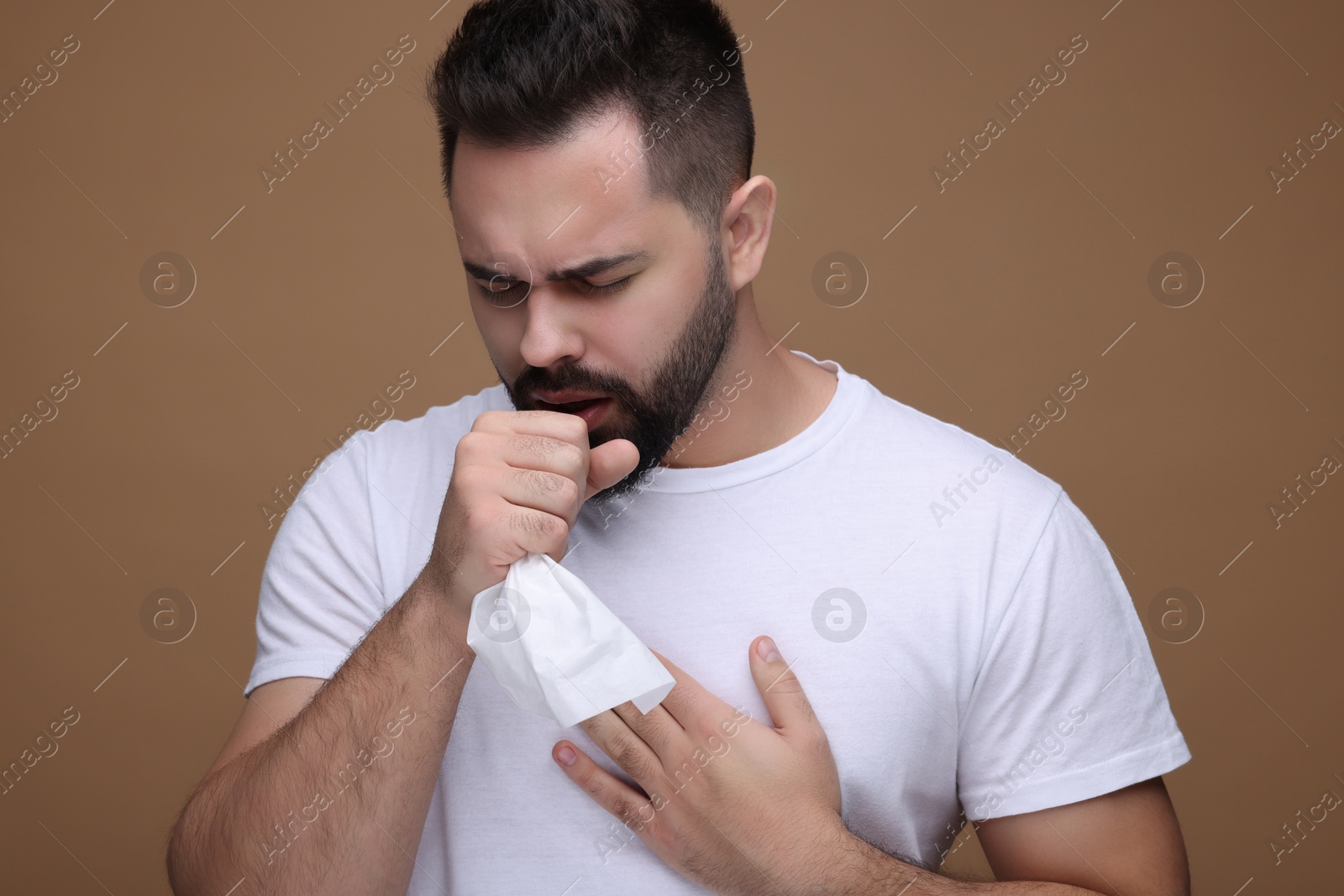 Photo of Sick man with tissue coughing on brown background