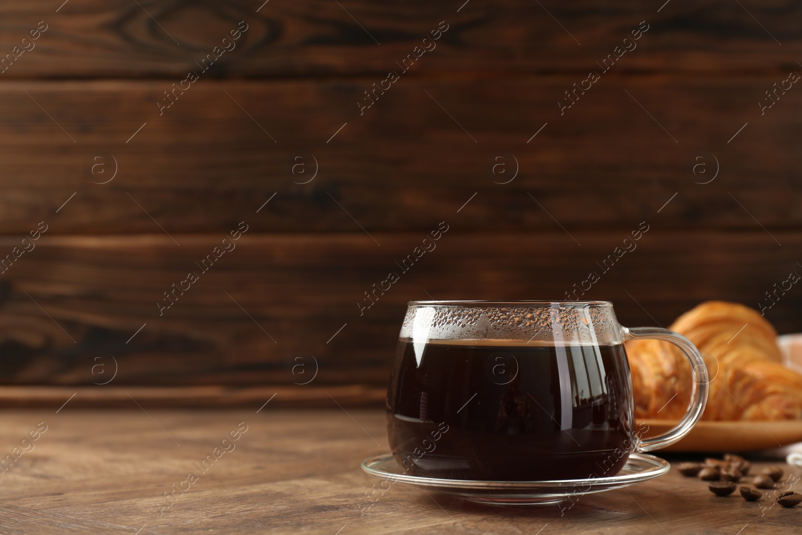 Photo of Hot coffee in glass cup and beans on wooden table, closeup. Space for text