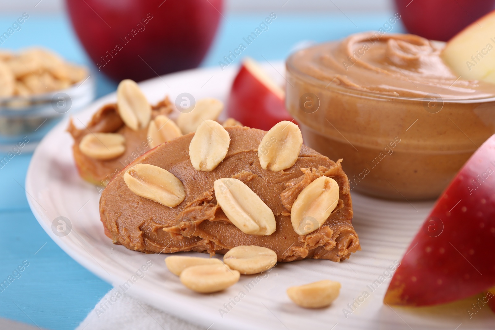 Photo of Slices of fresh apple with peanut butter and nuts on light blue table, closeup