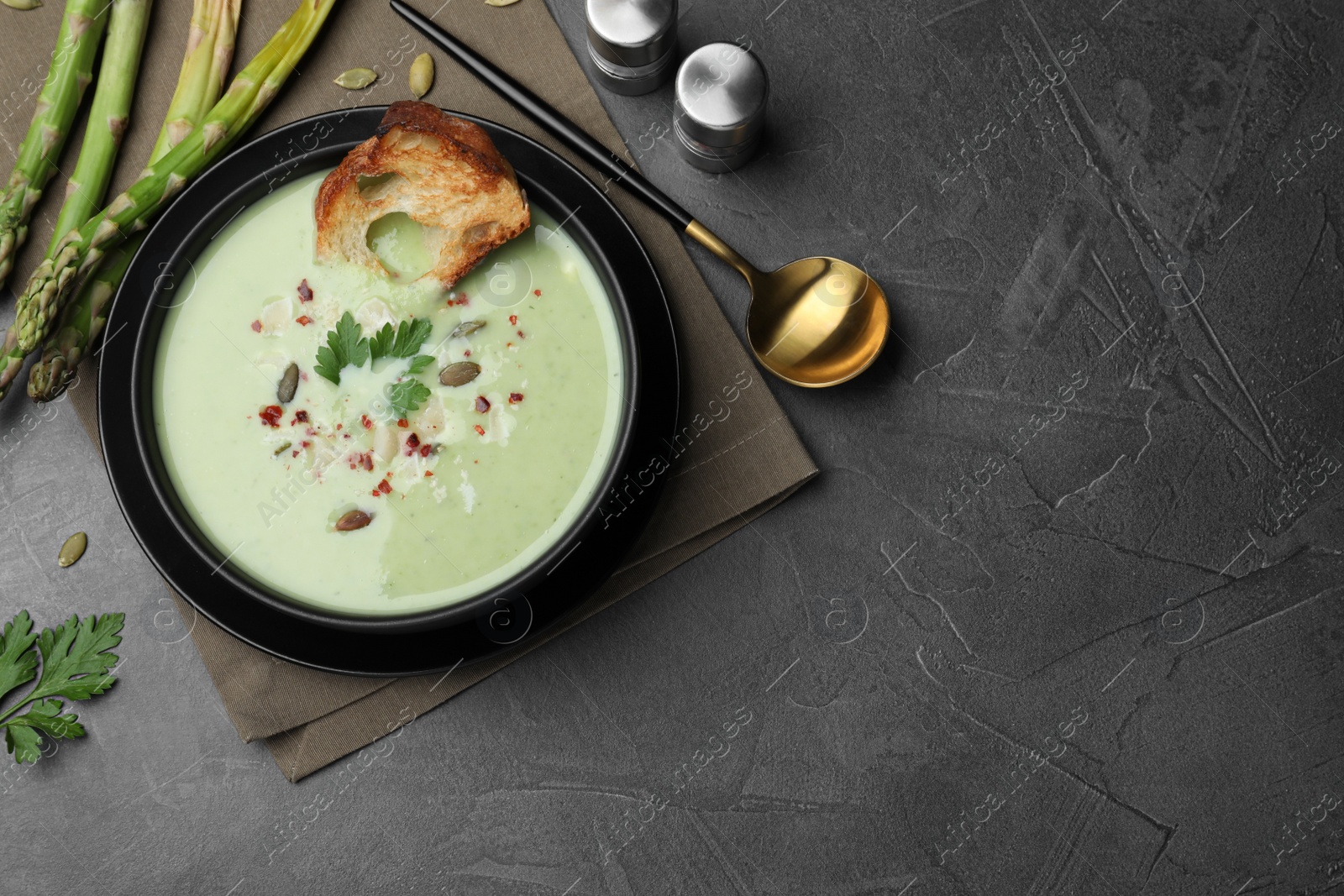 Photo of Bowl of delicious asparagus soup served on dark table, flat lay. Space for text