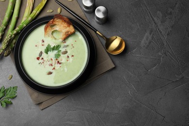 Bowl of delicious asparagus soup served on dark table, flat lay. Space for text