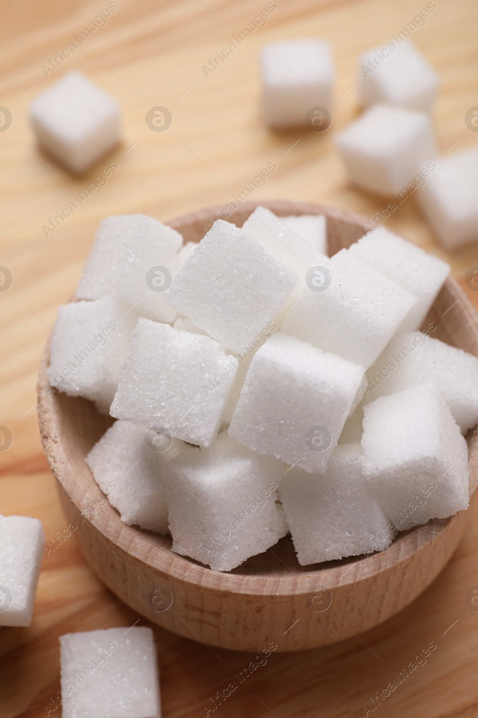 Photo of White sugar cubes in bowl on wooden table, above view