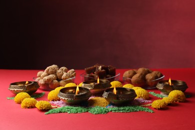 Happy Diwali. Diya lamps, colorful rangoli, flowers and delicious Indian sweets on red table