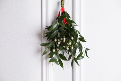 Photo of Mistletoe bunch with red ribbon hanging on light background. Traditional Christmas decoration