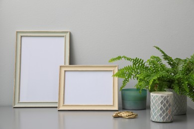Empty photo frames, candles and green plant on grey table