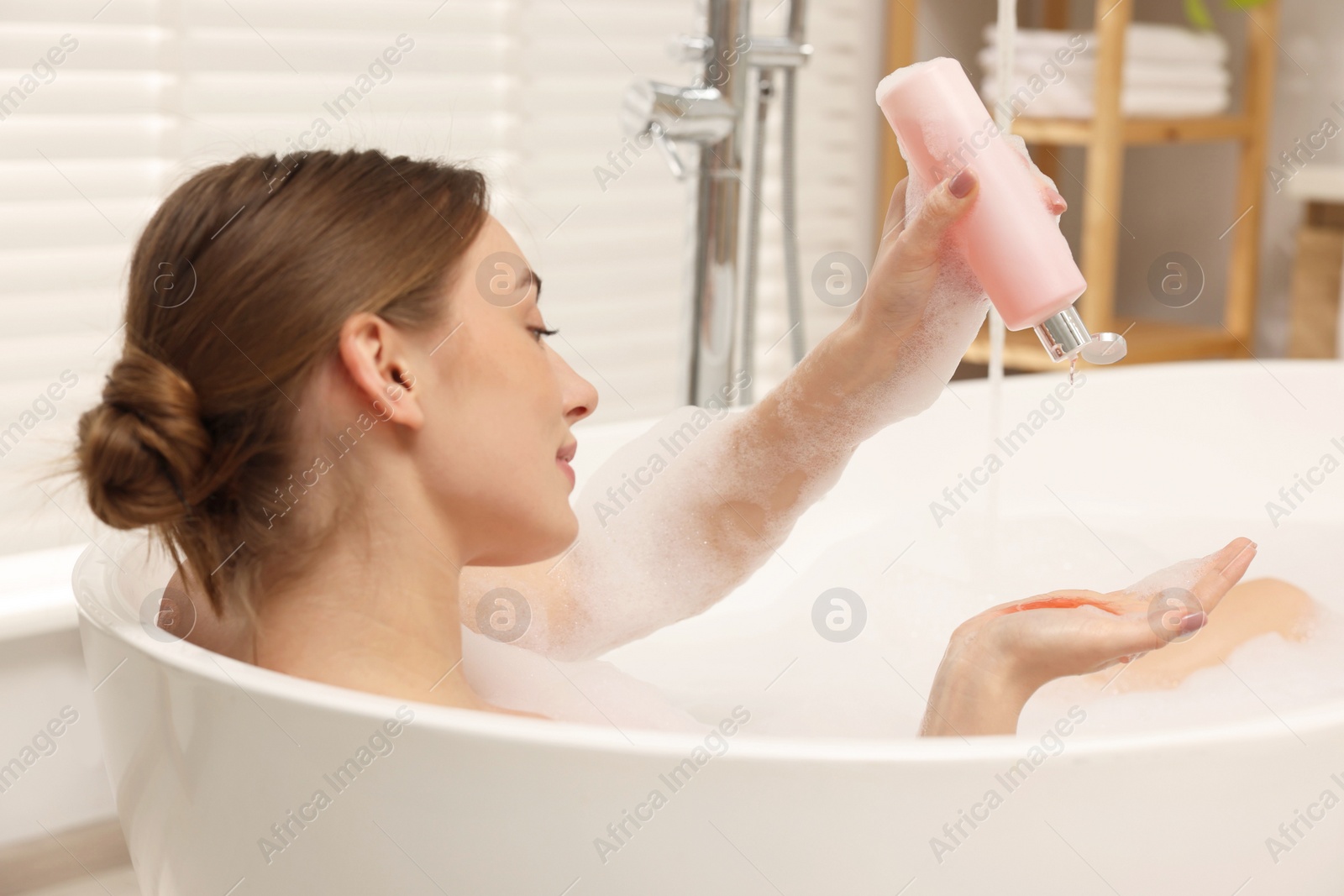 Photo of Woman pouring shower gel onto hand in bath indoors