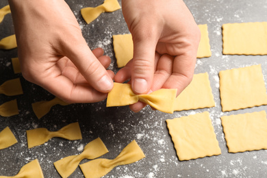 Photo of Woman making farfalle pasta at grey table, closeup