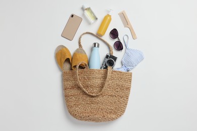 Wicker bag, smartphone and beach accessories on white background, flat lay