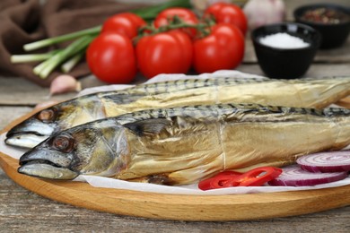 Photo of Delicious smoked mackerels, chili pepper and onion on wooden table, closeup